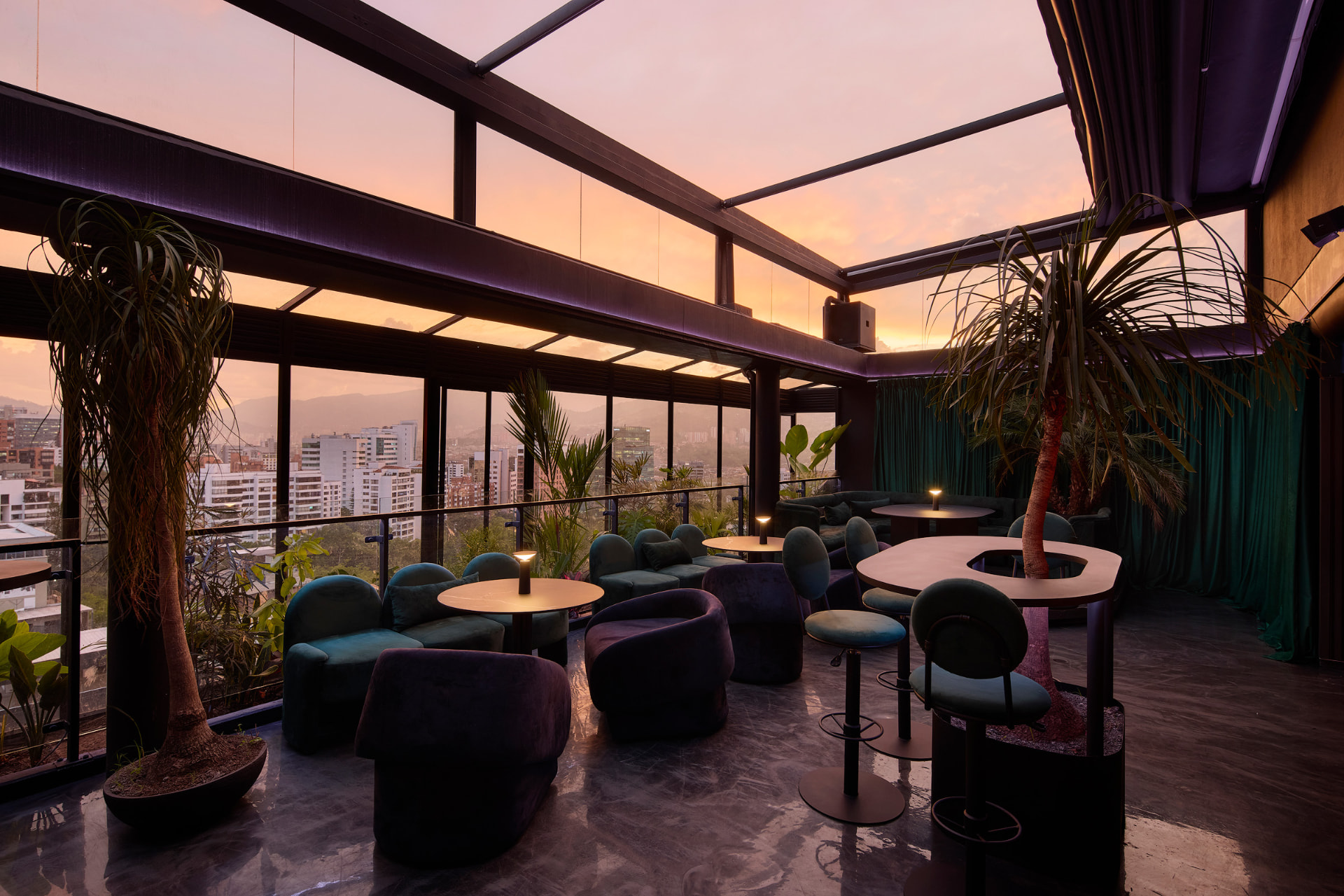 Terraza rooftop al atardecer con butacas en terciopelo verde y morado