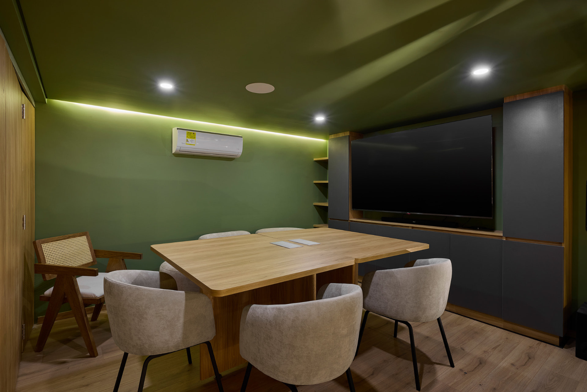 Sala de juntas verde con mesa en madera y sillones claros